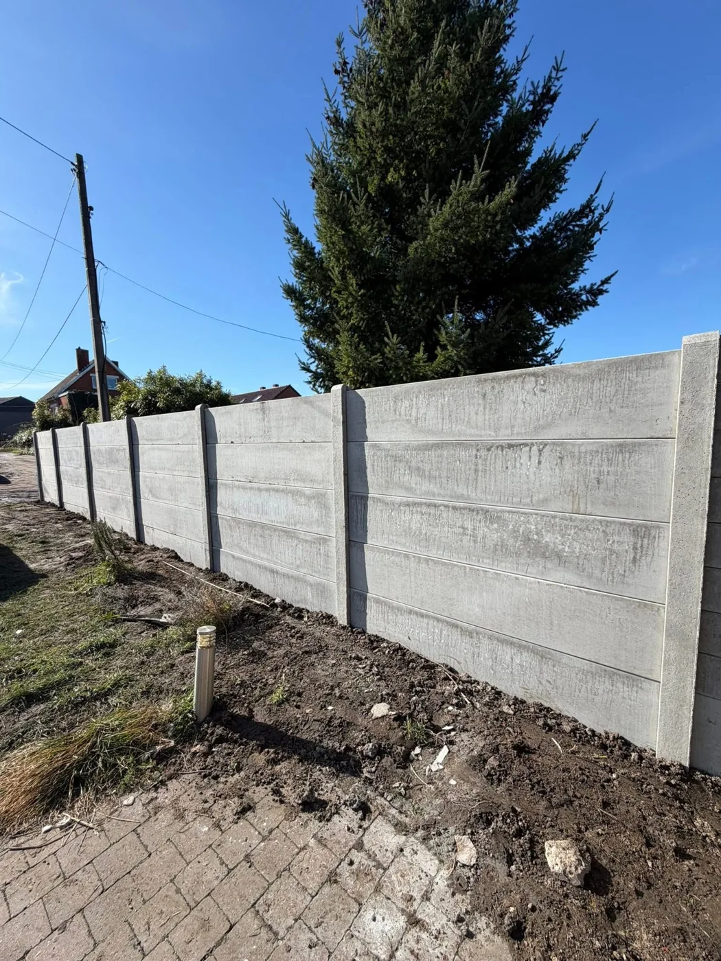 Clôture en panneaux de béton installée en bordure de jardin.